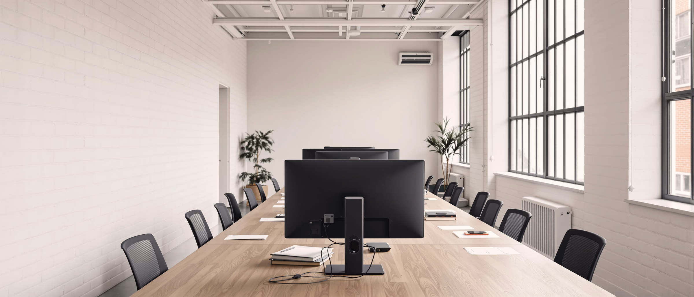 A long shared worktable running the length of a bright studio, monitors standing in a row along it